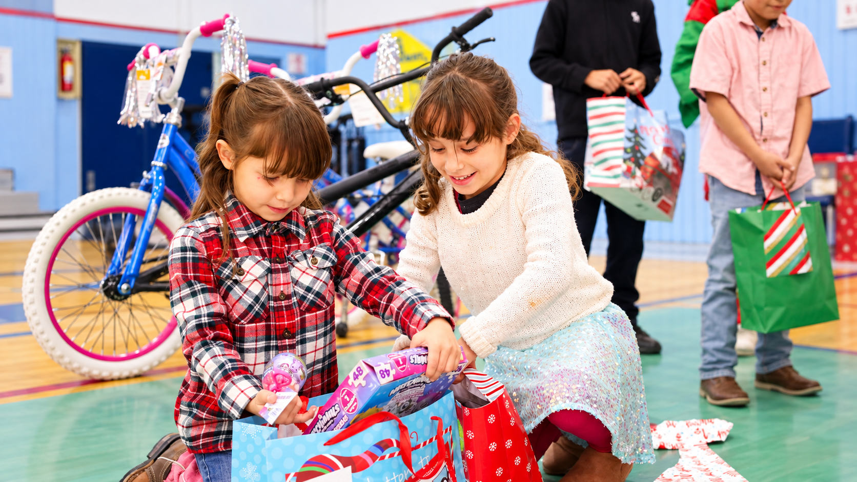 Two girls kneeling together and looking at wrapped gifts during a holiday outreach event