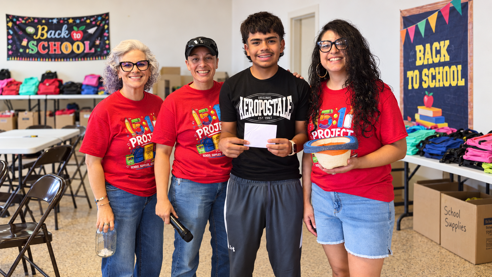 Volunteers and a student at a back-to-school supply event in a classroom setting